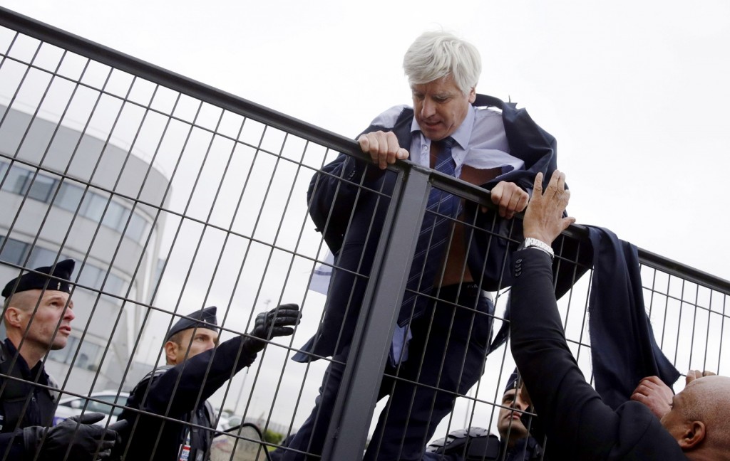 -- AFP PICTURES OF THE YEAR 2015 -- Director in charge of human resources of Air France long-haul flights, Pierre Plissonnier, nearly shirtless, is helped by security and police officers to climb over a fence, after several hundred employees stormed into the offices of Air France, interrupting the meeting of the Central Committee (CCE) in Roissy-en-France, on October 5, 2015. Air France-KLM unveiled a revamped restructuring plan on October 5 that could lead to 2,900 job losses after pilots for the struggling airline refused to accept a proposal to work longer hours. AFP PHOTO / KENZO TRIBOUILLARD / AFP / KENZO TRIBOUILLARD