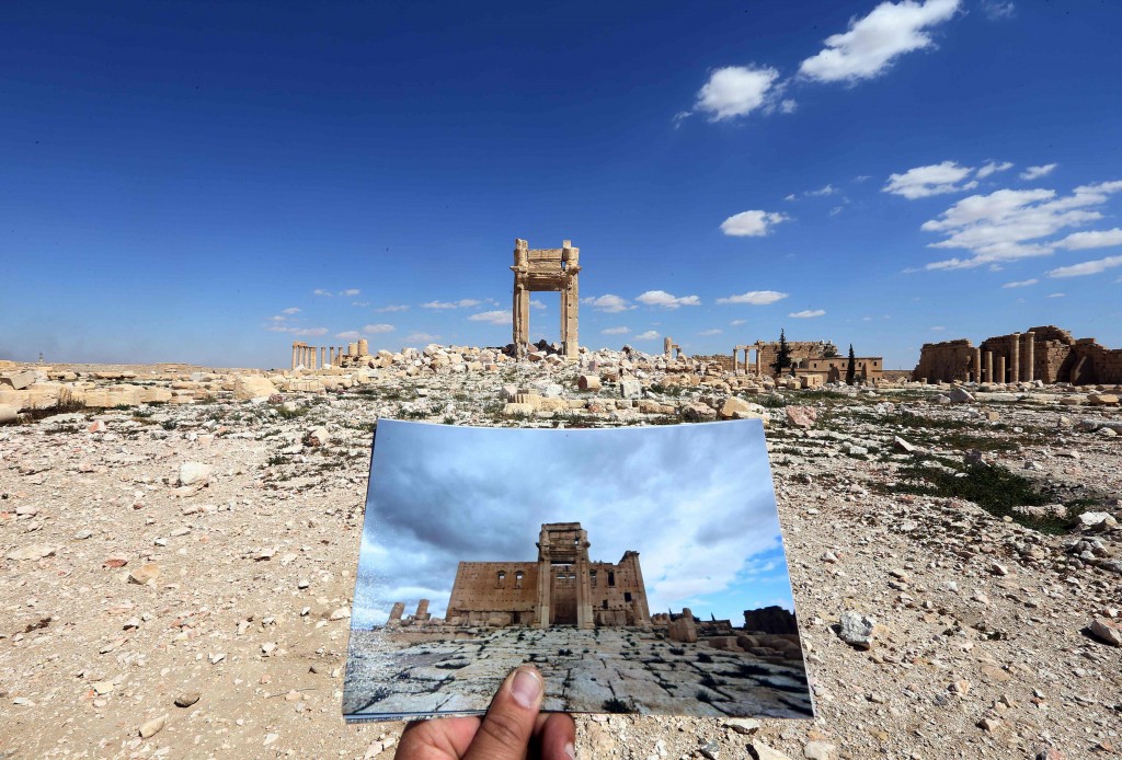 A general view taken on March 31, 2016 shows a photographer holding his picture of the Temple of Bel taken on March 14, 2014 in front of the remains of the historic temple after it was destroyed by Islamic State (IS) group jihadists in September 2015 in the ancient Syrian city of Palmyra. Syrian troops backed by Russian forces recaptured Palmyra on March 27, 2016, after a fierce offensive to rescue the city from jihadists who view the UNESCO-listed site's magnificent ruins as idolatrous. / AFP / JOSEPH EID